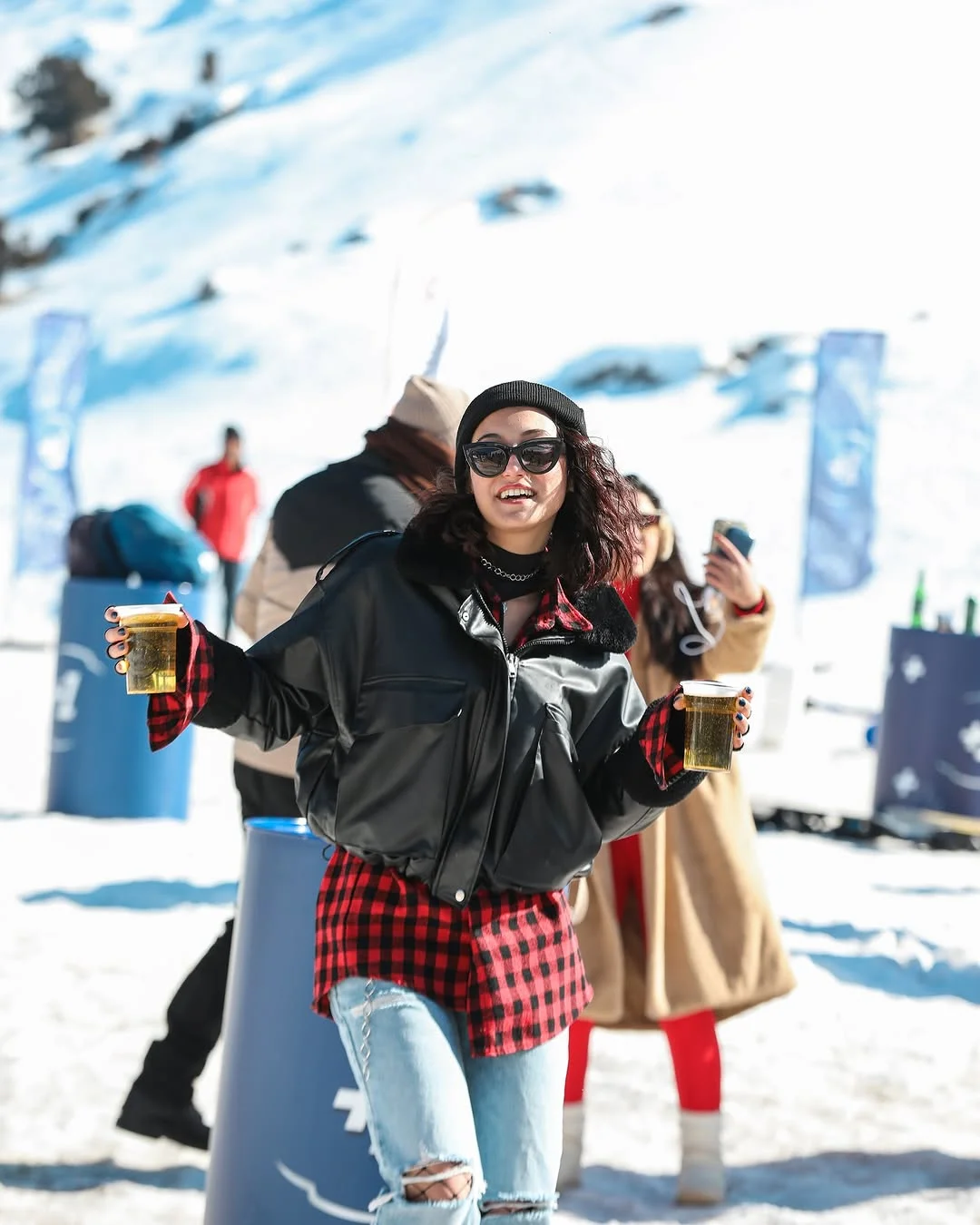 Festival katılımcıları elinde içecekle kar üzerinde eğlenirken